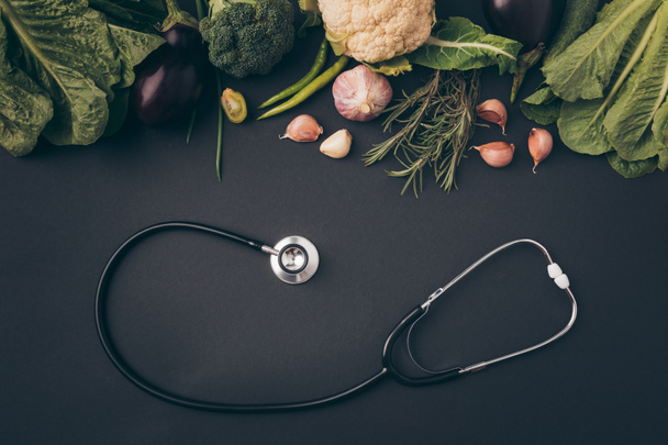 top view of stethoscope with green vegetables on gray table - Φωτογραφία, εικόνα