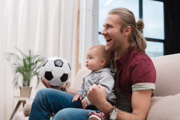 взволнованный отец с маленьким мальчиком смотреть футбольный матч дома
 - Фото, изображение