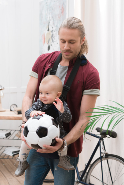 father with son in baby sling holding a football ball - Photo, Image