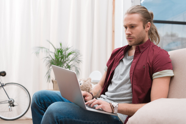 Handsome man sitting on sofa at home and looking at laptop - Photo, Image