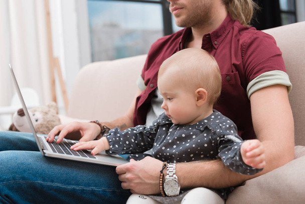 cropped view of father sitting with little baby girl and using laptop - Valokuva, kuva