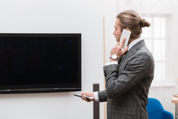 Homme d'affaires parler par smartphone et allumer la télévision à la maison
   - Photo, image
