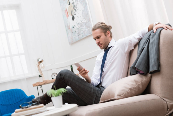 homme d'affaires sérieux utilisant un smartphone assis sur le canapé à la maison
 - Photo, image