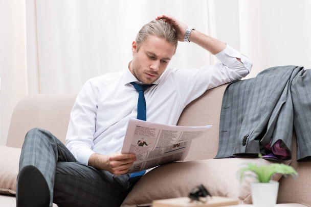 skoncentrowane biznesmen czytanie gazety na kanapie w domu - Zdjęcie, obraz