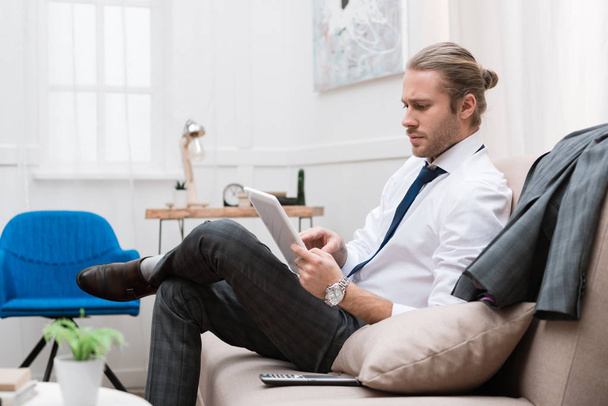 businessman using digital tablet while sitting on sofa at home - Foto, imagen