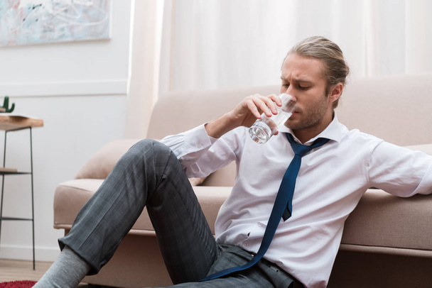 Businessman sitting on a floor at home and drinking water - Fotografie, Obrázek