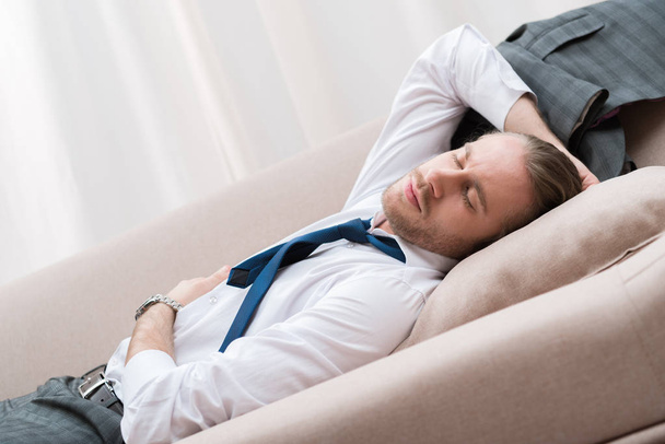 Уставший бизнесмен спит на диване в рубашке и галстуке
 - Фото, изображение