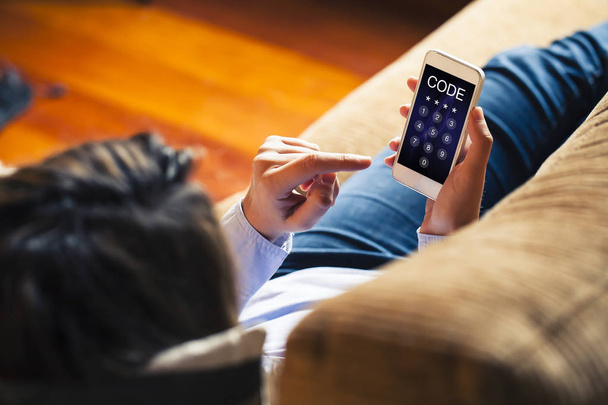 Woman entering unlocking code in a mobile phone while lies down on a sofa at home. - Foto, imagen