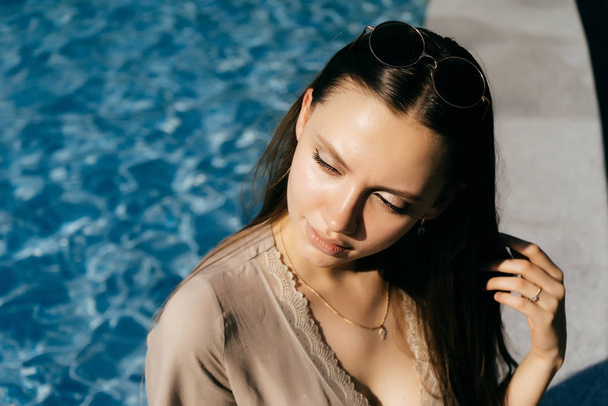 young girl model posing in the sun, sitting by the pool with blue water - Fotó, kép