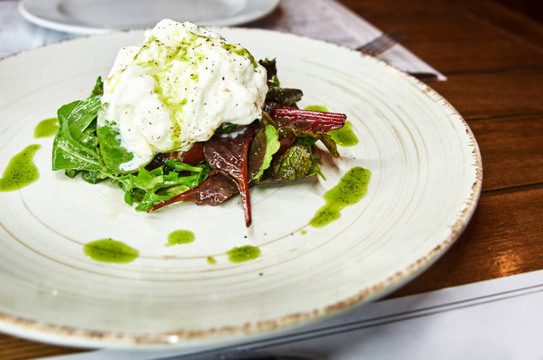 Traditional Italian specialty Burrata Cheese on ceramic plate served with olive oil and green salad over a white rustic wooden table. - Foto, Bild