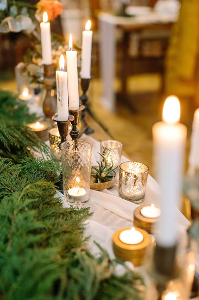 christmas, celebrating, dinner concept. lights of burning candles create atmosphere of comfort and cosiness, and fresh green branches of conifers are placed nearby - Foto, imagen