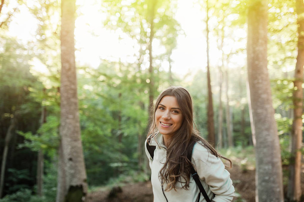 Young woman resting after a walk in the forest, carrying a backpack in the forest on sunset light in the autumn season. - Foto, imagen