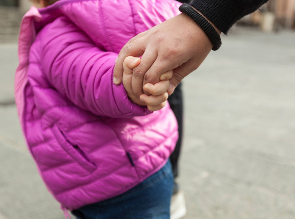 Toddler girl holding hands with her mother in a winter day. Concept of danger. - Photo, Image