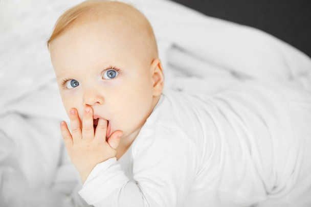 Baby with dreamy look lies on bed with finger in mouth - Fotoğraf, Görsel