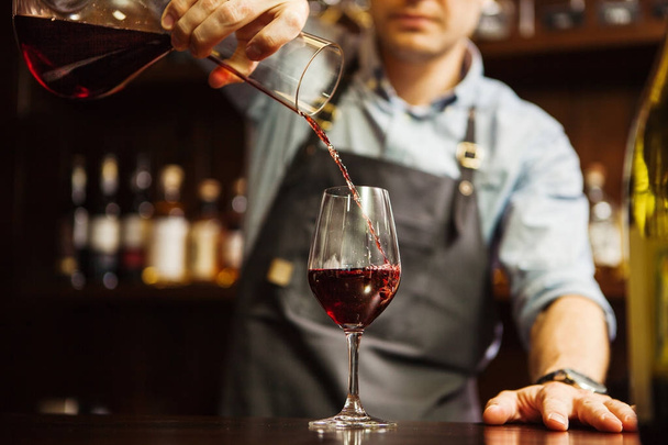 Şarap garsonu karıştırma kabından bardağa şarap dolduruyor. Erkek garson. - Fotoğraf, Görsel