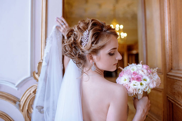 Beauty bride in bridal gown with bouquet and lace veil indoors - Fotó, kép