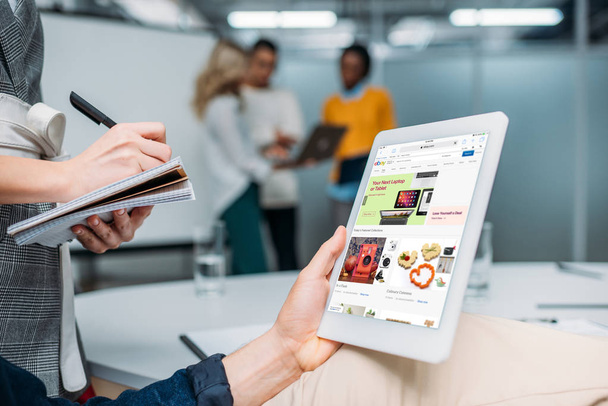 podnikatel hospodářství tablet s ebay na obrazovce v moderní kanceláři a kolega poznámky - Fotografie, Obrázek