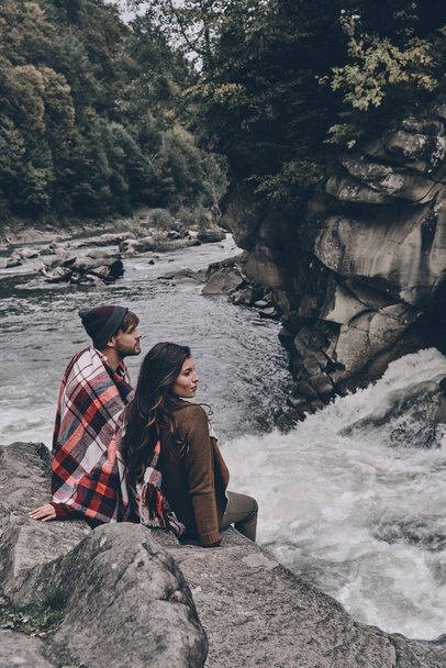 couple covered with blanket sitting on rocks - Zdjęcie, obraz