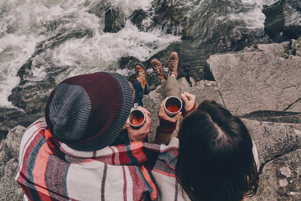 couple covered with blanket sitting on rocks - Фото, изображение
