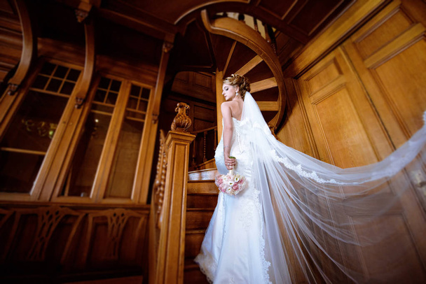 Beauty bride in bridal gown with bouquet and lace veil indoors - Foto, afbeelding
