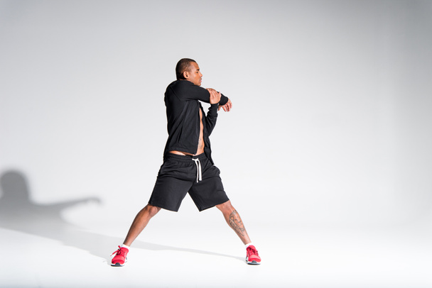 full length view of young athletic african american sportsman stretching on grey - Foto, Imagen