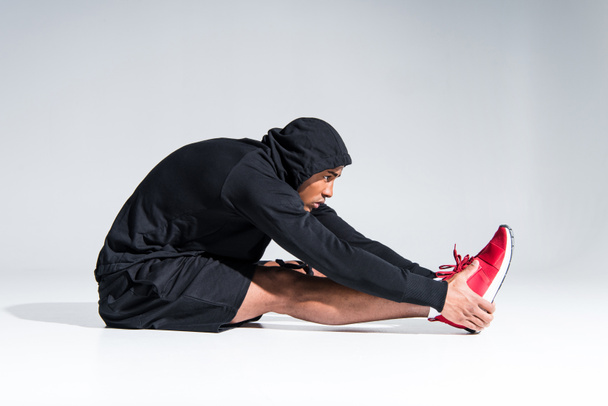 side view of young african american sportsman stretching on grey - Foto, Imagen