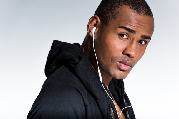 young african american man listening music in earphones and looking at camera isolated on grey - Foto, imagen