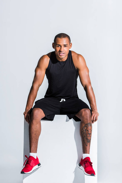 young african american sportsman in sportswear sitting and smiling at camera on grey - Foto, afbeelding