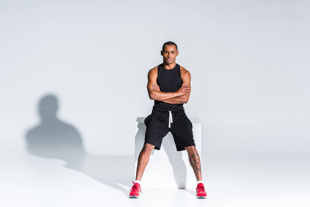 oturma ve gri kameraya bakarak çapraz kolları olan genç Afro-Amerikan sporcu - Fotoğraf, Görsel
