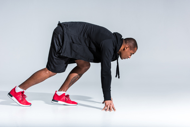 vista lateral do jovem esportista afro-americano com capuz pronto para correr em cinza
 - Foto, Imagem