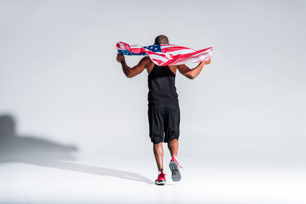 vista trasera del joven deportista afroamericano sosteniendo bandera americana en gris
 - Foto, Imagen