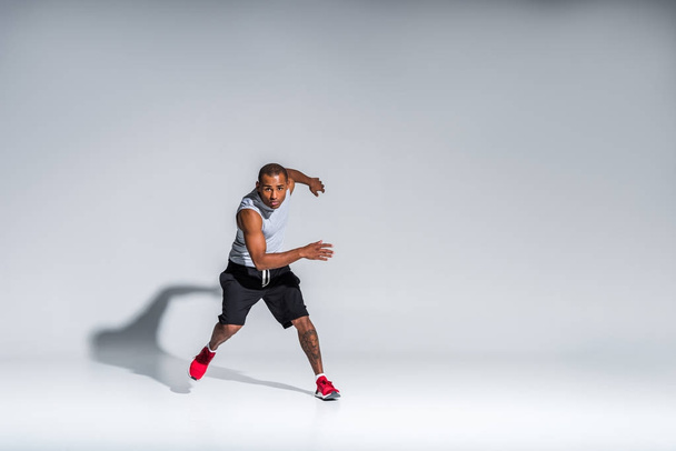 volle lengte weergave van atletische jonge Afro-Amerikaanse sportman camera kijken op grijs - Foto, afbeelding