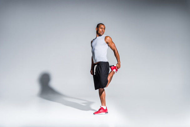 jonge Afro-Amerikaanse sportman rekken en kijkt weg op grijs - Foto, afbeelding