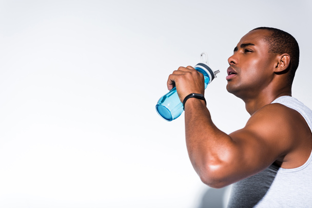 young african american sportsman drinking water from sports bottle on grey - Photo, Image