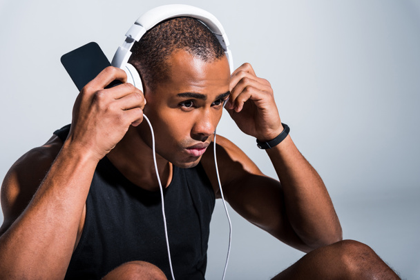 young african american sportsman in headphones using smartphone and looking away on grey - Valokuva, kuva