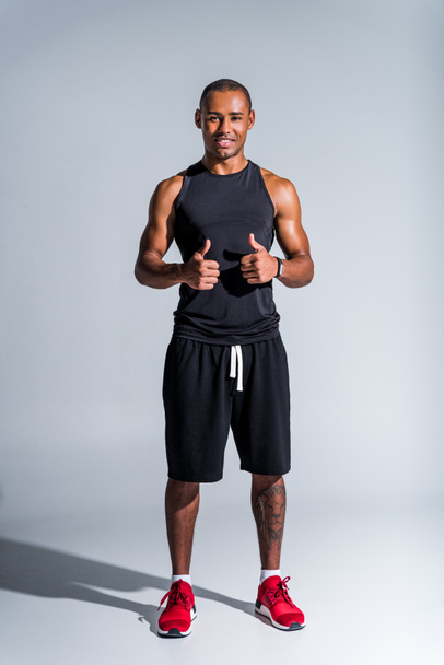 cheerful african american sportsman showing thumbs up and smiling at camera isolated on grey - Фото, зображення
