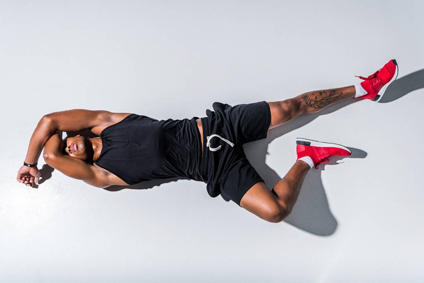вид зверху молодого афроамериканця з закритими очима в спортивному одязі і лежить на сірому
  - Фото, зображення