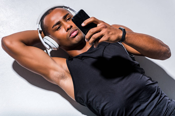 young african american man in headphones using smartphone on grey  - Photo, Image