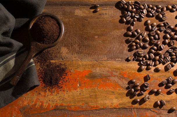 Donker geroosterde zuivere arabica koffiebonen en gemalen koffie in oude lepel op de houten tafel, kopie ruimte - Foto, afbeelding
