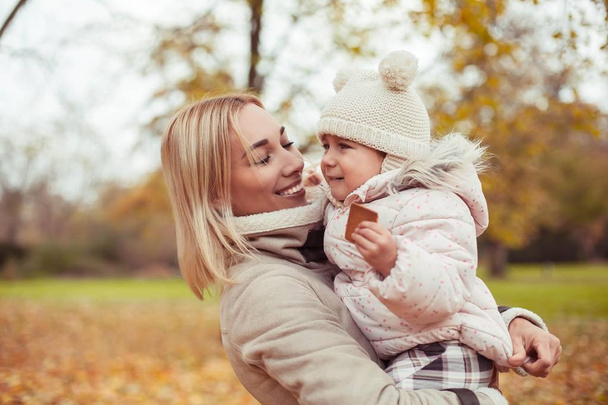 Молода мама і маленька донька ходять восени. Мама і дочка грають. Тепла зима. Яскрава осінь
. - Фото, зображення