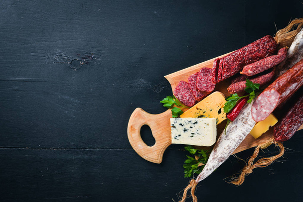Assortment of cheeses and traditional sausages on a wooden background. Brie cheese, blue cheese, gorgonzola, fuete, salami. Free space for text. Top view. - Foto, Imagem