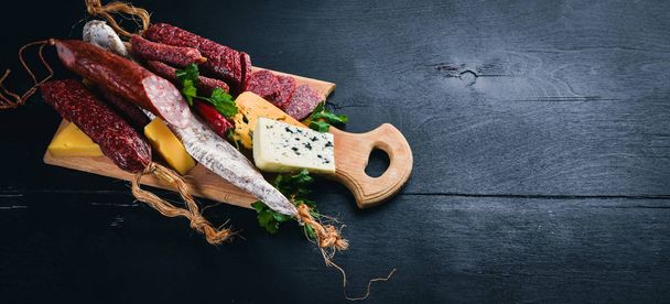 Assortment of cheeses and traditional sausages on a wooden background. Brie cheese, blue cheese, gorgonzola, fuete, salami. Free space for text. Top view. - Foto, Imagem