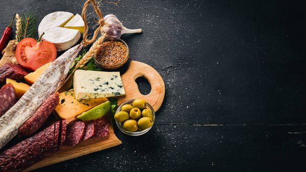 Assortment of cheeses and traditional sausages on a wooden background. Brie cheese, blue cheese, gorgonzola, fuete, salami. Free space for text. Top view. - Photo, image