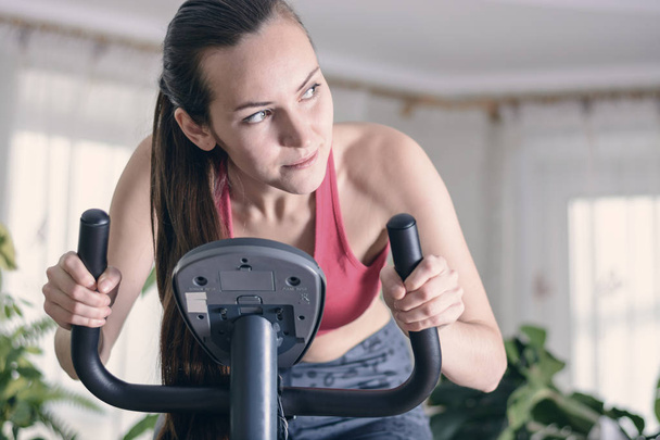 Европейская женщина тренирует кардио тренировки дома на велотренажере. Концепция потери веса. Мотивированная и целеустремленная девушка
 - Фото, изображение