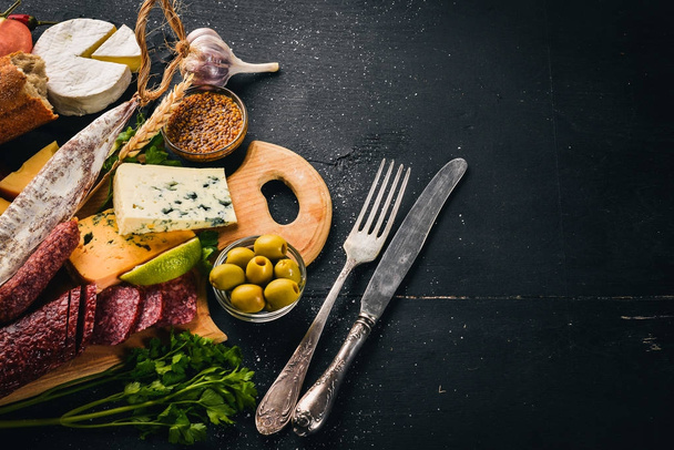 Assortment of cheeses and traditional sausages on a wooden background. Brie cheese, blue cheese, gorgonzola, fuete, salami. Free space for text. Top view. - Photo, image