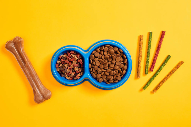 Dog food in blue bowl and accessories on yellow background - Photo, Image