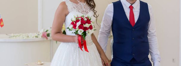Νύφης και του γαμπρού κρατώντας γαμήλια ανθοδέσμη με τριαντάφυλλα - Φωτογραφία, εικόνα