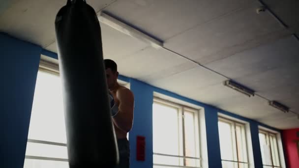 Gespierde man bokser treinen door bokszak op de sportschool in ontbloot bovenlijf bokshandschoenen. - Video
