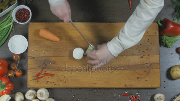 De chef-kok snijdt uien en wortelen. Uien en wortelen als ingrediënt voor het maken van soep of een andere schotel. Bovenaanzicht - Video