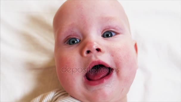 Slow motion portrait of blue-eyed baby boy smiling to someone behind the camera - Footage, Video